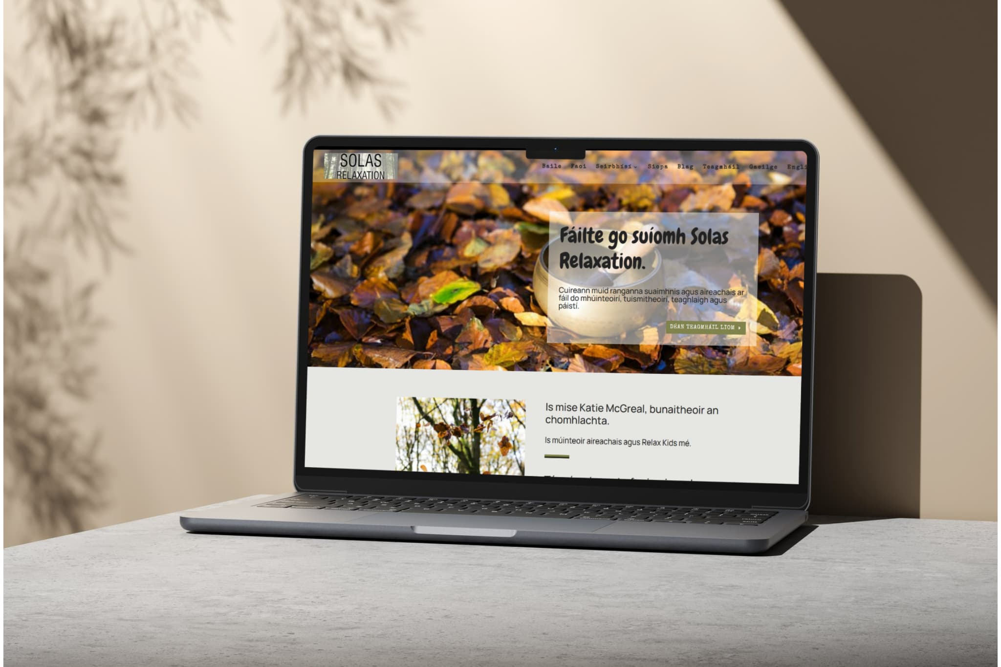 A laptop on a grey table displays a beautifully redesigned website with autumn leaves in the background. The text, primarily in Irish, warmly welcomes users to Solas Relaxation.