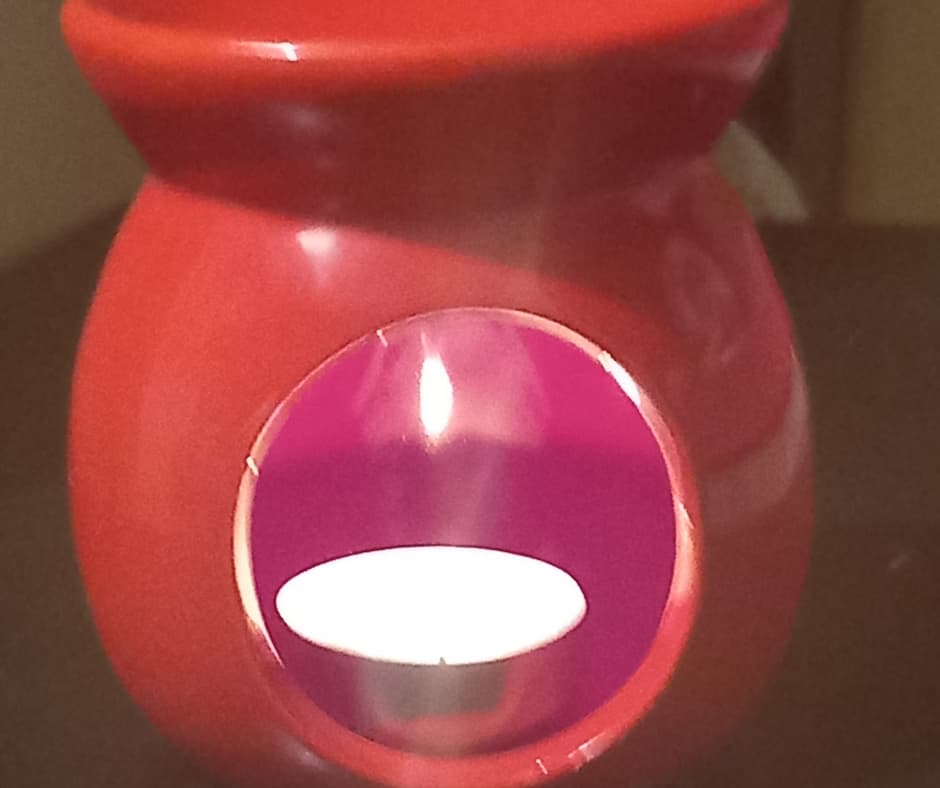 Red ceramic candle holder with a hollow centre, displaying a lit tealight candle inside. The holder has a glossy finish and a round opening.